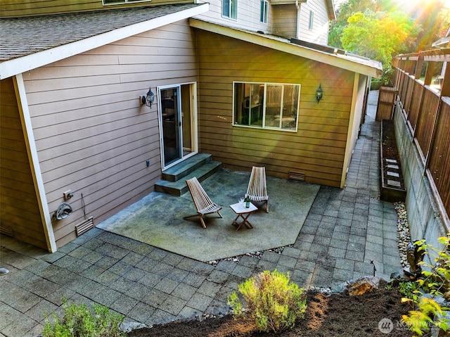 rear view of house featuring entry steps, fence, a patio, and a shingled roof