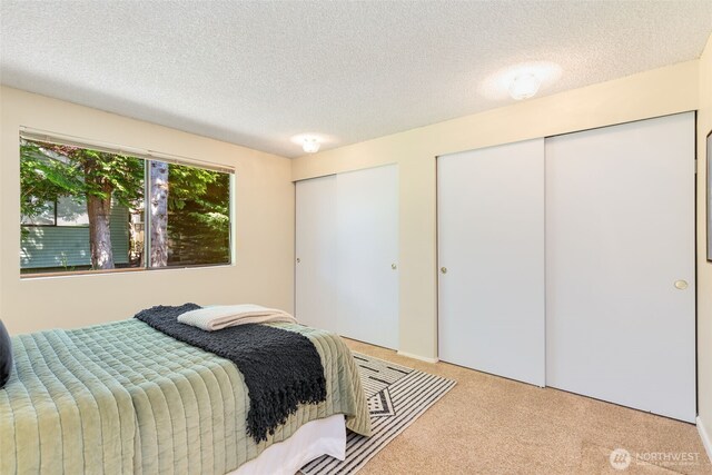 bedroom with multiple closets, light colored carpet, and a textured ceiling