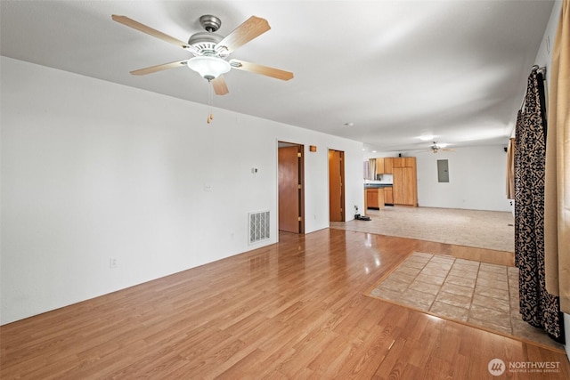 unfurnished living room with visible vents, a ceiling fan, light wood-style flooring, and electric panel
