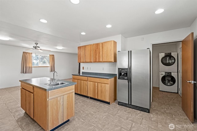 kitchen featuring stacked washer / dryer, an island with sink, ceiling fan, stainless steel refrigerator with ice dispenser, and a sink