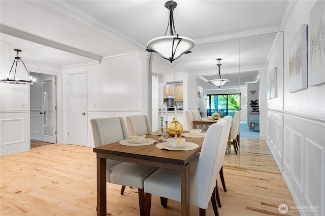 dining area featuring an inviting chandelier, ornamental molding, wainscoting, a decorative wall, and light wood-type flooring
