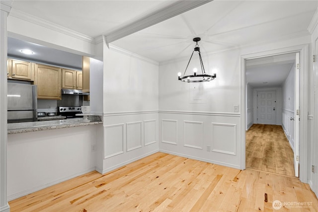 unfurnished dining area with a wainscoted wall, an inviting chandelier, ornamental molding, a decorative wall, and light wood-style flooring