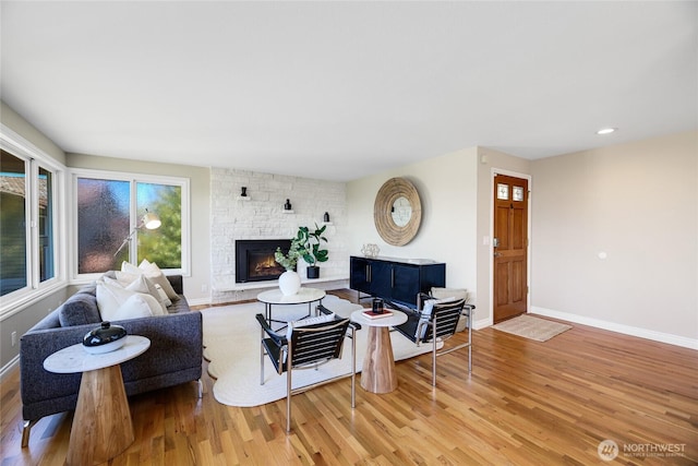 living area featuring a stone fireplace, recessed lighting, baseboards, and wood finished floors