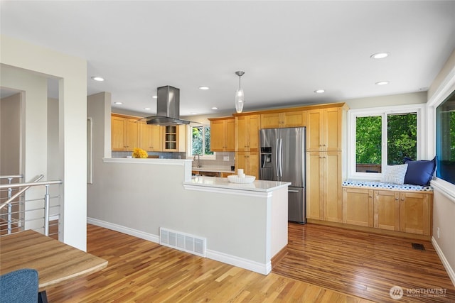kitchen featuring light wood finished floors, a peninsula, island exhaust hood, stainless steel refrigerator with ice dispenser, and visible vents
