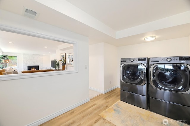 laundry area with visible vents, a fireplace, baseboards, light wood-style floors, and washer and dryer