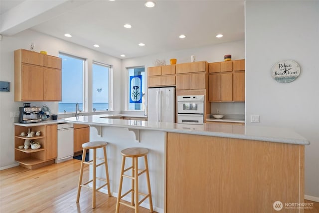 kitchen featuring open shelves, a breakfast bar, light wood finished floors, white appliances, and light countertops