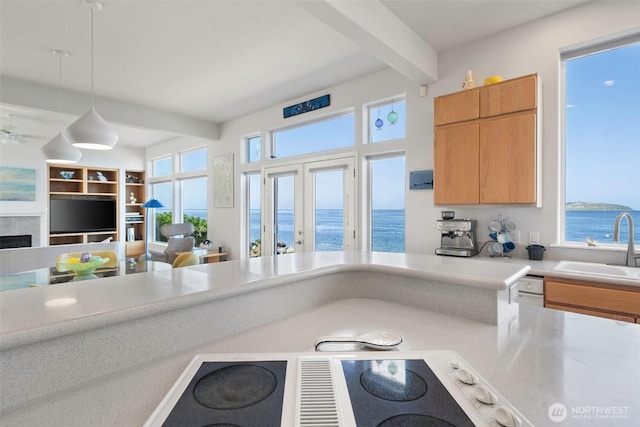 kitchen featuring pendant lighting, beam ceiling, a sink, light countertops, and a water view