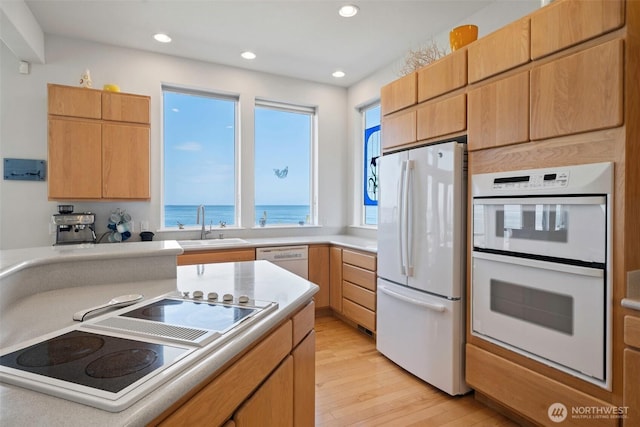 kitchen with a sink, light countertops, light wood finished floors, recessed lighting, and white appliances