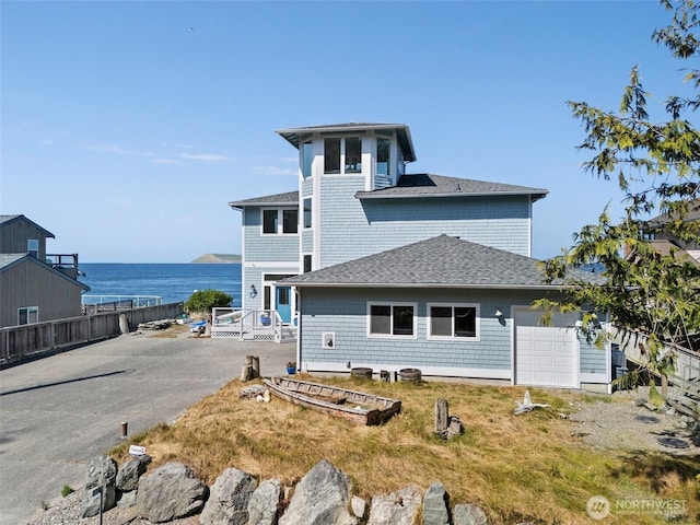 exterior space featuring an attached garage, a water view, fence, aphalt driveway, and roof with shingles