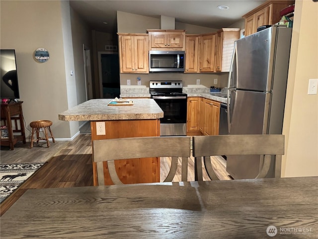 kitchen with appliances with stainless steel finishes, a center island, light countertops, lofted ceiling, and dark wood-type flooring
