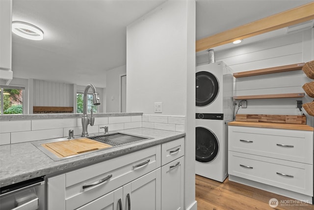 laundry room featuring a sink, light wood-style floors, stacked washer and clothes dryer, and laundry area