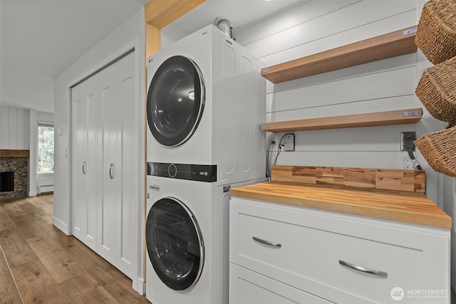laundry room featuring stacked washer / dryer, a fireplace, cabinet space, a baseboard radiator, and light wood-style floors