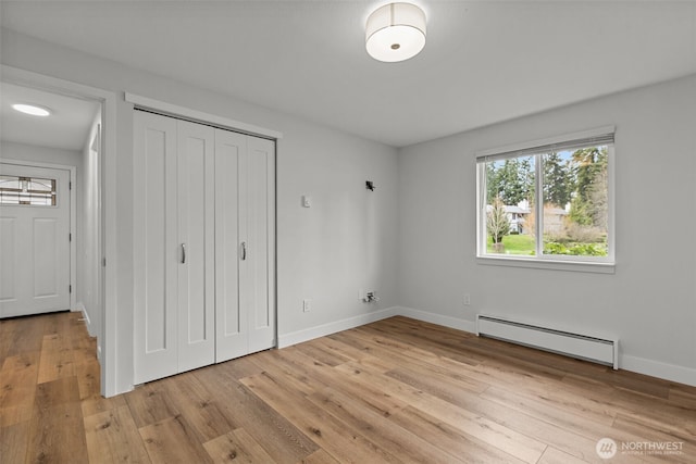 unfurnished bedroom with a closet, baseboards, a baseboard heating unit, and light wood-type flooring