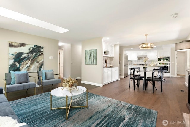 living room with baseboards, dark wood-type flooring, recessed lighting, a notable chandelier, and a skylight