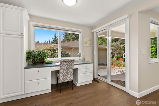 unfurnished office with a healthy amount of sunlight, baseboards, built in desk, and dark wood-type flooring