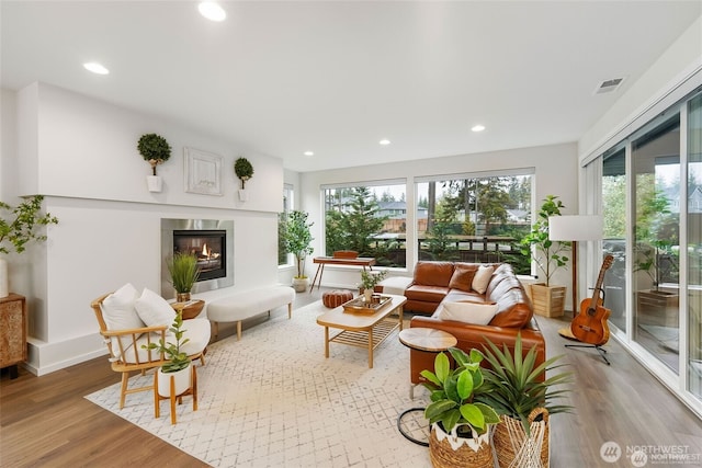 living area featuring a glass covered fireplace, recessed lighting, plenty of natural light, and light wood finished floors