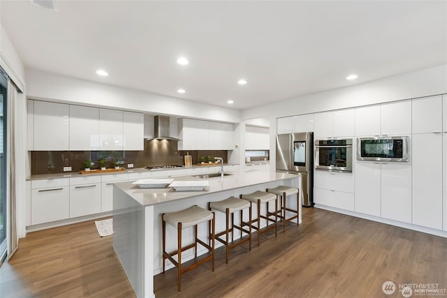 kitchen featuring a sink, a breakfast bar area, wall chimney exhaust hood, stainless steel appliances, and modern cabinets