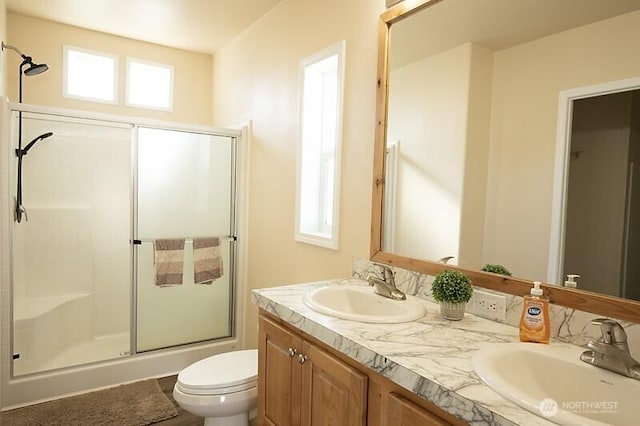 full bathroom with double vanity, a sink, a shower with door, and toilet