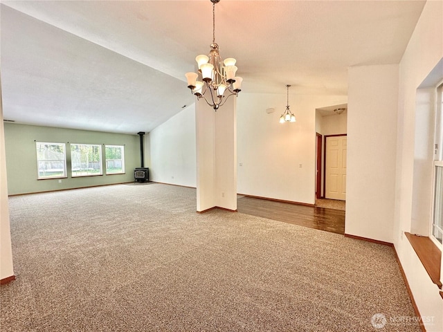 spare room with a wood stove, vaulted ceiling, baseboards, an inviting chandelier, and carpet