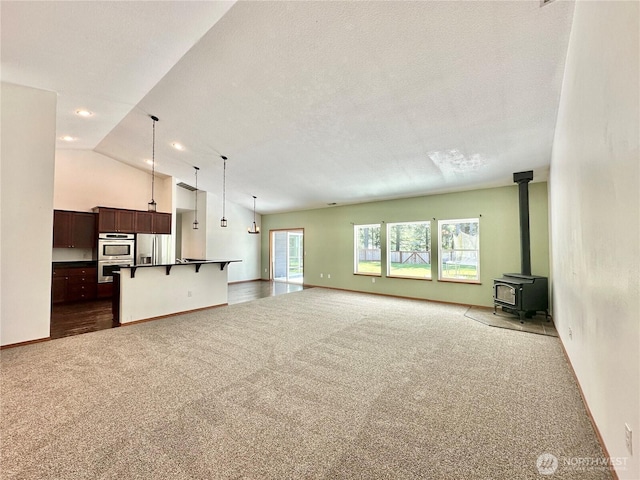 unfurnished living room with visible vents, a wood stove, dark colored carpet, baseboards, and high vaulted ceiling