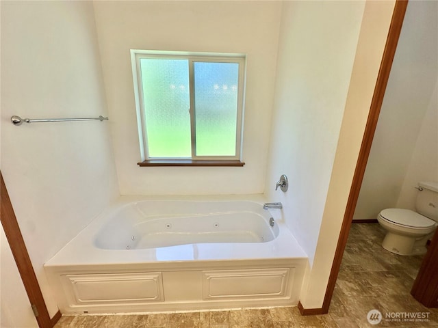 bathroom with baseboards, a tub with jets, and toilet