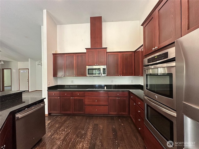 kitchen with reddish brown cabinets, dark wood finished floors, dark countertops, and stainless steel appliances