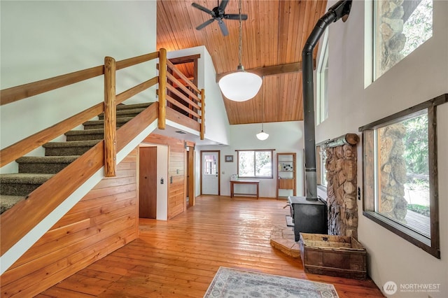 living area featuring high vaulted ceiling, a ceiling fan, a wood stove, and hardwood / wood-style floors