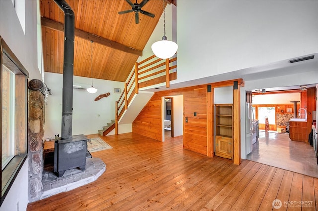 unfurnished living room featuring ceiling fan, a wood stove, high vaulted ceiling, beamed ceiling, and hardwood / wood-style floors