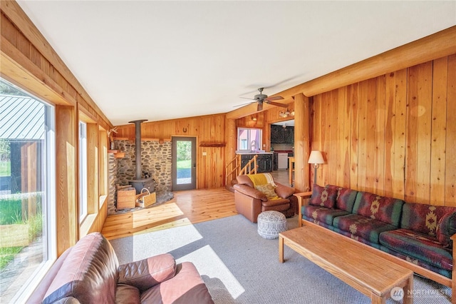 carpeted living room featuring ceiling fan, a wood stove, wood walls, and lofted ceiling