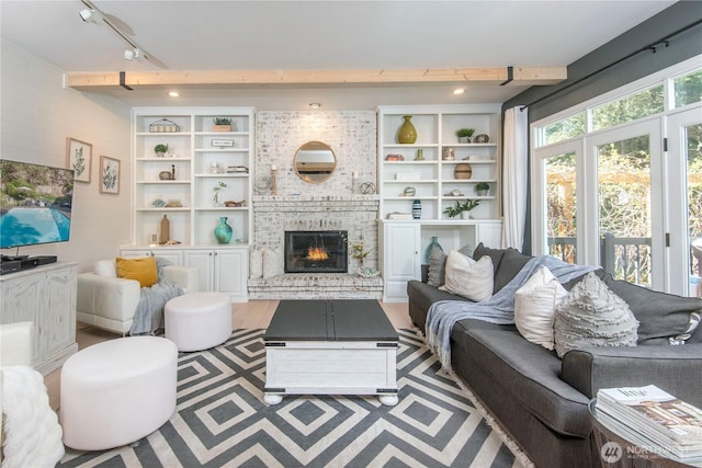living area featuring track lighting, a brick fireplace, wood finished floors, and beamed ceiling
