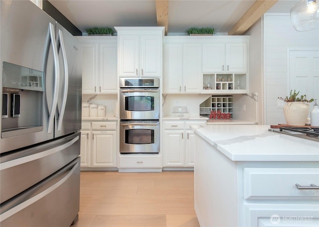 kitchen with white cabinetry, beamed ceiling, appliances with stainless steel finishes, and light wood finished floors