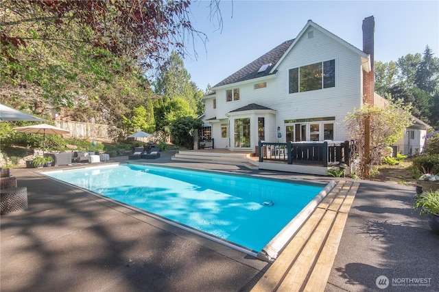 rear view of house featuring a deck, a fenced in pool, a chimney, an outdoor living space, and a patio area