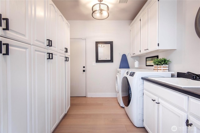 laundry room with baseboards, light wood-type flooring, separate washer and dryer, a sink, and cabinet space