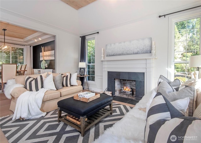 living room with a fireplace with flush hearth, a raised ceiling, ornamental molding, and wood finished floors