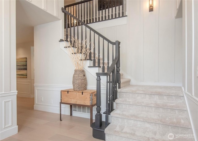 staircase with wood finished floors, a decorative wall, and a wainscoted wall
