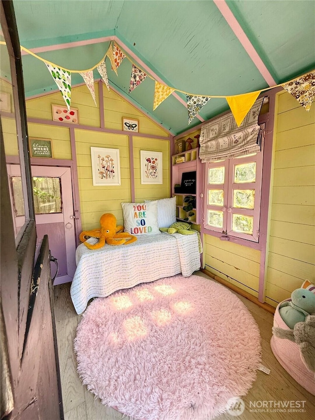 bedroom with vaulted ceiling, wood walls, and wood finished floors