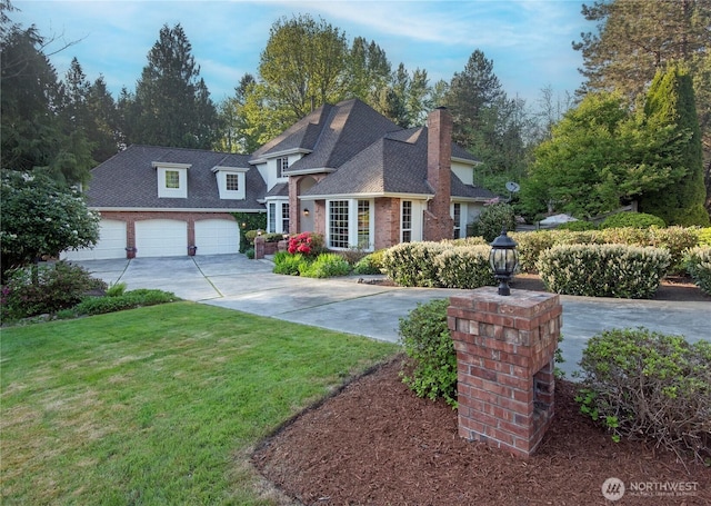 traditional-style home featuring a garage, a chimney, a front yard, brick siding, and driveway