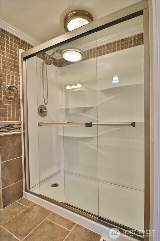 bathroom featuring tile patterned floors, tile walls, a shower stall, and ornamental molding