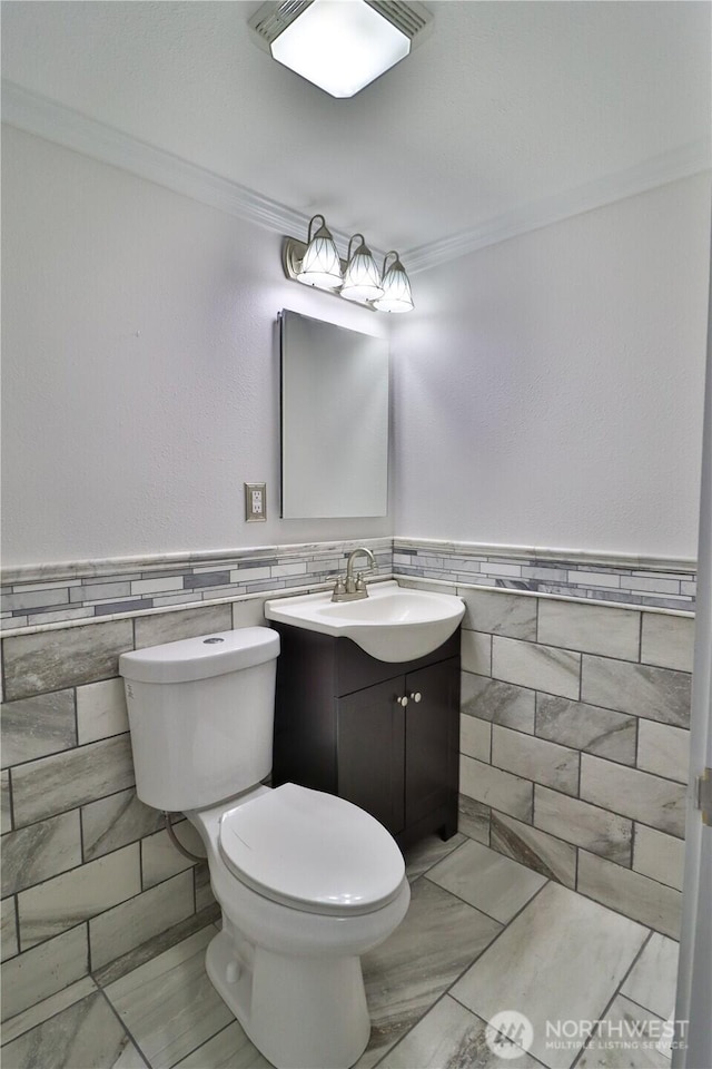 half bathroom with crown molding, tile walls, vanity, and toilet