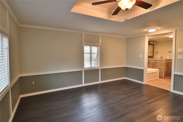 spare room with dark wood-style flooring, ceiling fan, baseboards, a tray ceiling, and ornamental molding