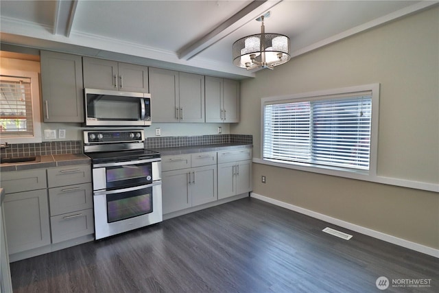 kitchen featuring dark wood-style flooring, beam ceiling, a sink, appliances with stainless steel finishes, and gray cabinetry