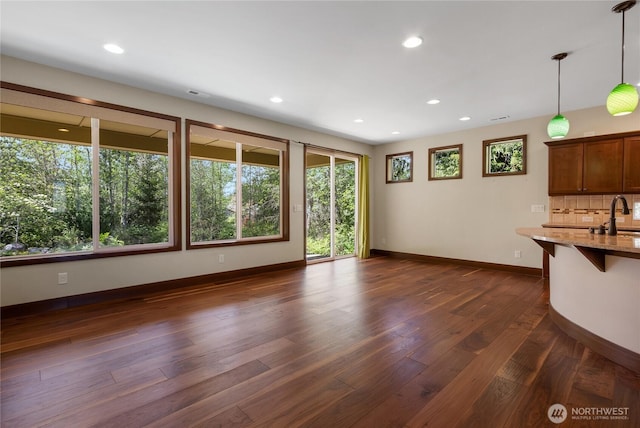 unfurnished living room featuring baseboards, dark wood finished floors, plenty of natural light, and a sink