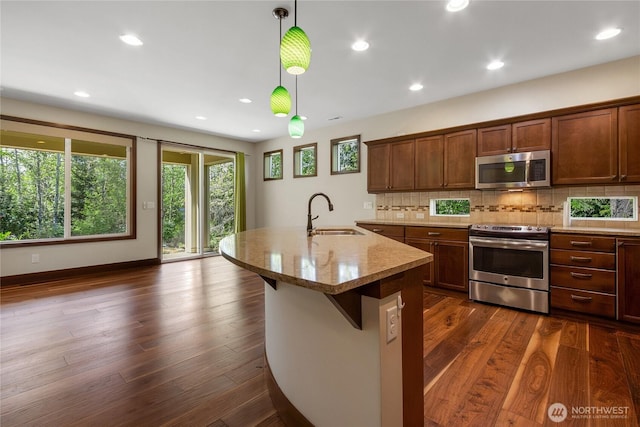 kitchen featuring pendant lighting, appliances with stainless steel finishes, tasteful backsplash, light stone countertops, and a sink