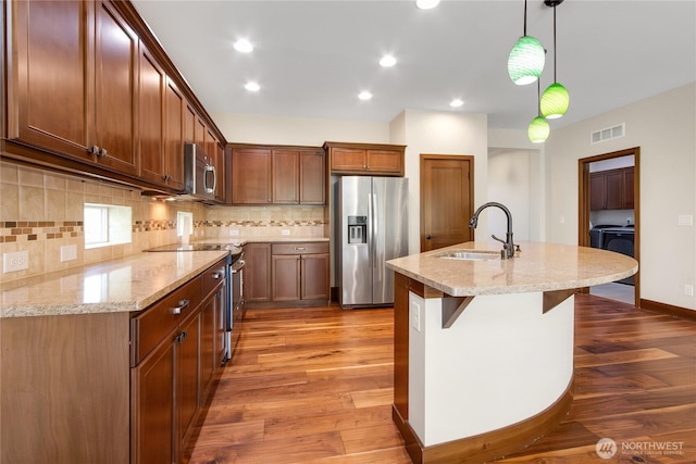 kitchen with visible vents, decorative backsplash, washing machine and dryer, a sink, and stainless steel appliances
