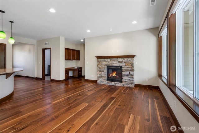 unfurnished living room with dark wood-style flooring, baseboards, visible vents, and a stone fireplace