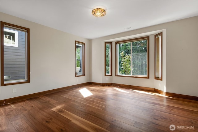 unfurnished room with baseboards, wood finished floors, and visible vents