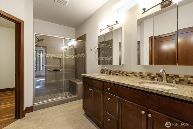 bathroom featuring a sink, a stall shower, double vanity, and visible vents