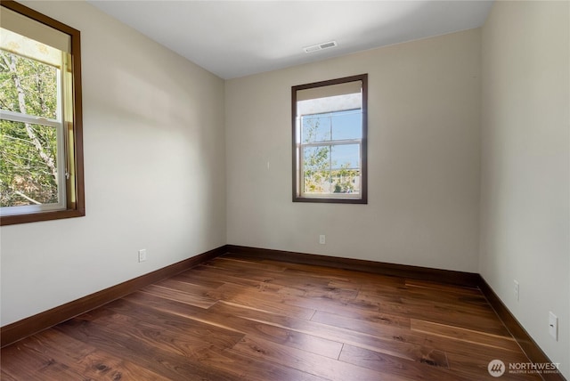 empty room featuring visible vents, a healthy amount of sunlight, and dark wood-type flooring
