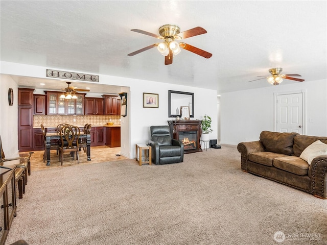 living room featuring a glass covered fireplace, ceiling fan, and light carpet
