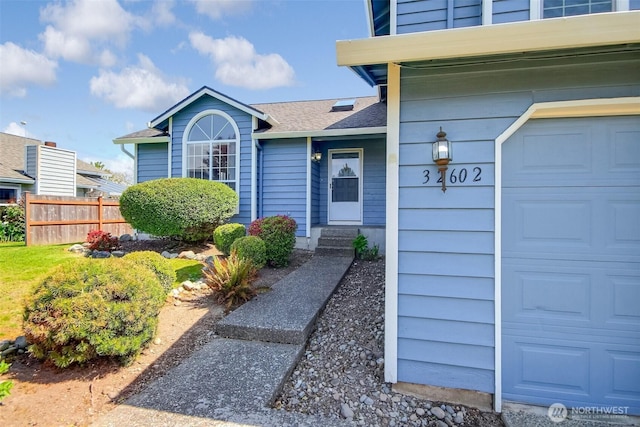 view of exterior entry with fence, roof with shingles, and a garage